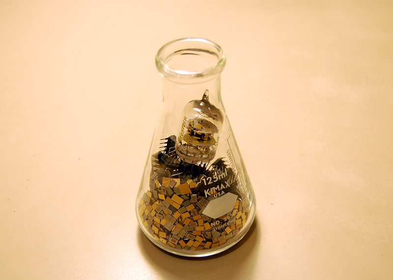 A lab flask containing IC's, raw silicon chips, and a vacuum tube